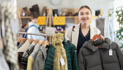 Focused female client carefully looking down jacket for autumn-winter season in big clothing mall. Black Friday sale of winter clothing collection