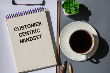 Top view of magnifying glass,pen and notebook written with Customer Centric Mindset on wooden background.