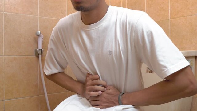 Man sitting on toilet holding stomach in pain