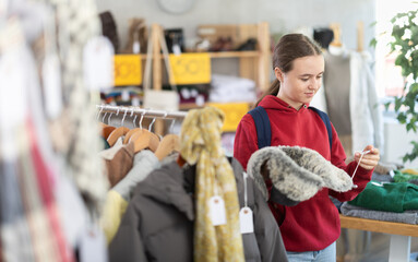Teenage girl chooses a winter fur hat with interest, she holds it in her hands and examines it....