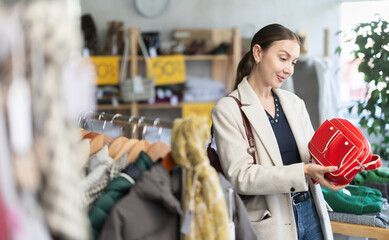 Happy young woman choosing ladies handbag in clothing shop during winter sale season