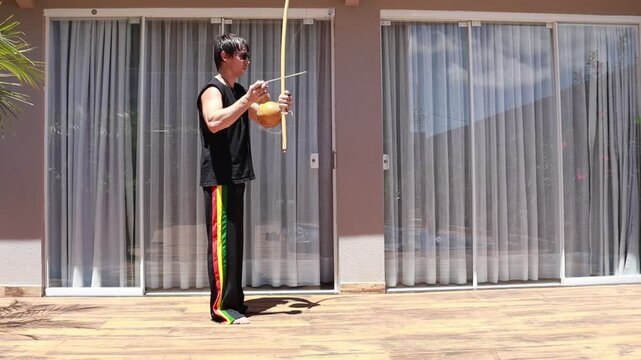 homem toca birimbau de capoeira em casa
