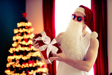Festive Santa in Sunglass Holding a Gift Box by a Decorated Christmas Tree in Warm Holiday Room