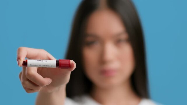 A millennial Asian woman is confidently presenting a test tube labeled COVID-19 positive, showcasing a moment of health awareness.