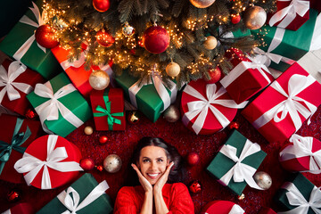 Festive young woman joyfully posing among colorful gift boxes under a bright Christmas tree in a cozy indoor setting