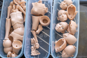 Closeup of silicone doll parts in containers, including various body and face pieces. Parts are awaiting assembly in the doll-making process
