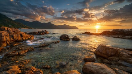 Obraz premium Golden sunlight reflects on calm waters as waves gently lap against rocky formations by the shore.