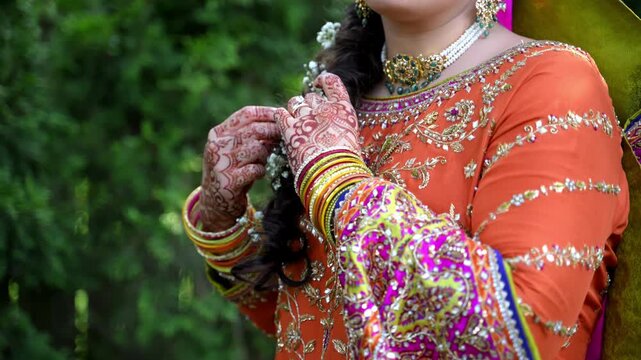 Close up view of Traditional Indian or Pakistan henna painted bridal hands with wedding rings. Bride playing with her braid decorated with flowers