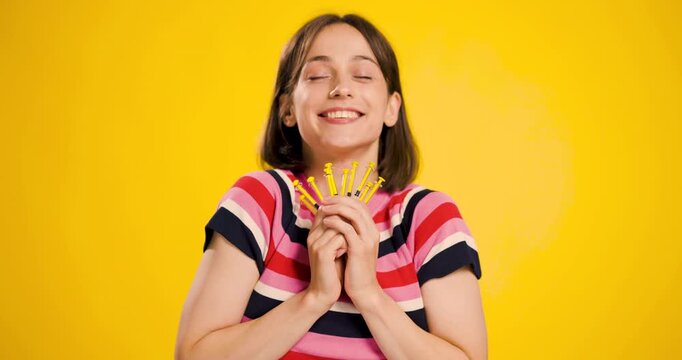 Joyful young woman holding yellow syringes with a content smile on a yellow background