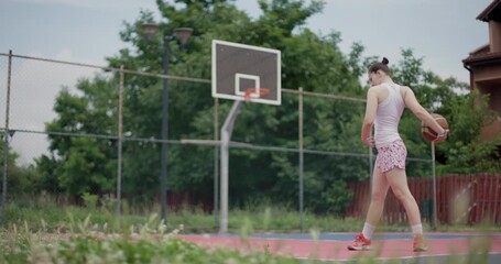 Female basketball player stretching with a ball on an outdoor court, preparing for a game with focus and determination - Powered by Adobe