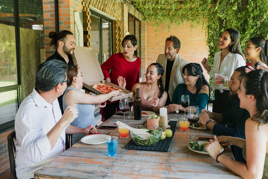 large group of friends or multi generation family eating pizza and having a dinner in a terrace party in Mexico Latin America, hispanic diverse and multicultural people in a restaurant - Powered by Adobe
