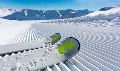 Skis on a freshly groomed corduroy slope, with majestic snow-capped mountains and a clear blue sky in a breathtaking winter landscape