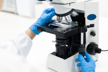 Selective focus woman Asian scientist using microscope to analyze blood smear slide sample at...