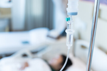 Close up set iv fluid intravenous drop saline drip in hospital room with blurry patient woman on hospital bed.Medical treatment emergency patient.Caregiver and hopeful concept.