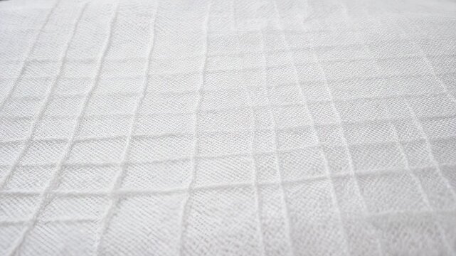 Detailed close-up of a white, textured fabric surface, featuring a subtle geometric grid pattern