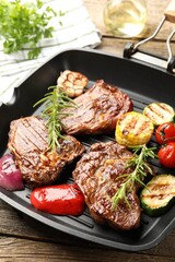 Pan with grilled beef steaks, rosemary and vegetables on wooden table, closeup