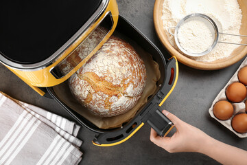 Woman opening air fryer with freshly baked bread at grey textured table, top view