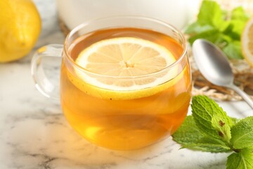 Aromatic tea in cup with lemon, mint and spoon on white marble table, closeup