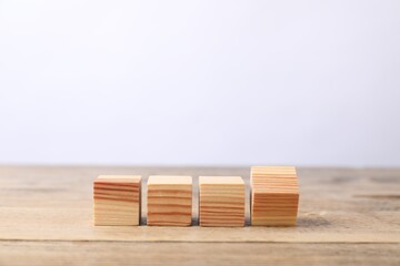 Blank cubes on wooden table against light background, space for text