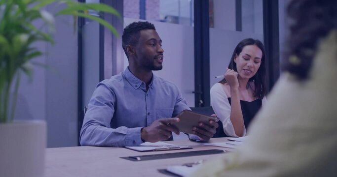 Man leading team holding tablet at table in meeting room, with pens, clipboards and potted plant - Powered by Adobe