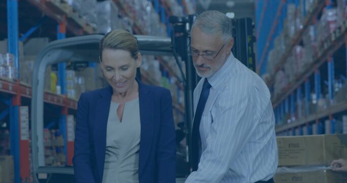 Colleagues wearing business attire checking boxes in warehouse aisle on shelving, with forklift