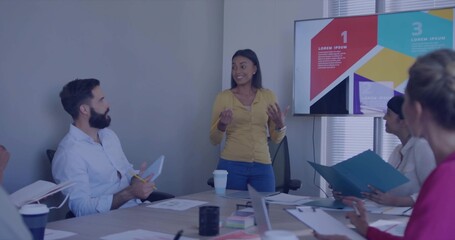 Presenting project manager wearing mustard blouse in conference room, with infographic and laptops