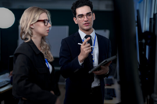 A senior software developer leads a code review session, pointing to a specific function on the screen to explain its logic and syntax to a junior engineer before a major deployment.