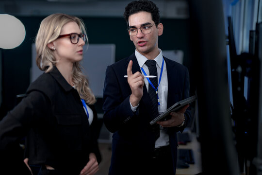 A senior software developer leads a code review session, pointing to a specific function on the screen to explain its logic and syntax to a junior engineer before a major deployment.