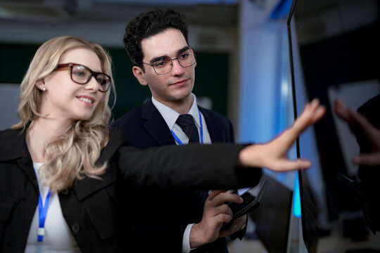 A senior software developer leads a code review session, pointing to a specific function on the screen to explain its logic and syntax to a junior engineer before a major deployment.