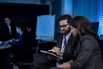 A diverse team of professionals collaborates on a business strategy late at night. A male manager...