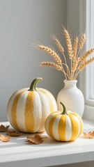 Photorealistic close-up of two pumpkins with white, soft orange, and yellow blended stripes; wheat stalk designs; matte cream vase, light gray wall, and natural window light