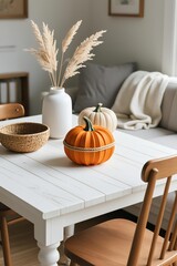 Cozy autumn scene with paper pumpkin, pampas grass in vase, woven jar, fabric pumpkin on white wooden table, gray pillow and blanket in background
