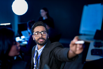 A diverse team of professionals collaborates on a business strategy late at night. A male manager uses a tablet and stylus to explain key points to his female colleague in a modern boardroom.
