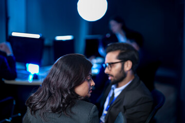 A diverse team of professionals collaborates on a business strategy late at night. A male manager uses a tablet and stylus to explain key points to his female colleague in a modern boardroom.