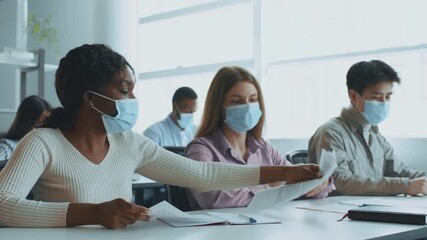In a bright classroom, diverse college students wear masks while collaborating on a project. They exchange notes and ideas, emphasizing teamwork and education in a university setting. - Powered by Adobe