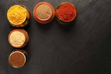 Overhead top view flat lay colourful array of spices herbs powder blue clay ceramic brass metal pot on dark black slate surface with a clean and neat appearance spice copy text space border frame