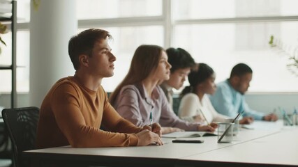 A diverse group of college students sits at a long table, concentrating on their studies. - Powered by Adobe
