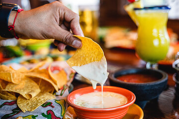 hand dipping a tortilla chip in queso cheese dip at a Mexican restaurant