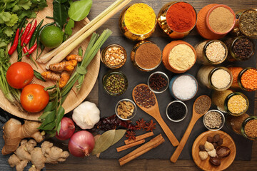Overhead flat lay vibrant colourful spices herbs fresh produce vegetables legumes on wooden table spread splash smoking spice mix dark black slate metal clay pot palm leaf plate board copy text frame