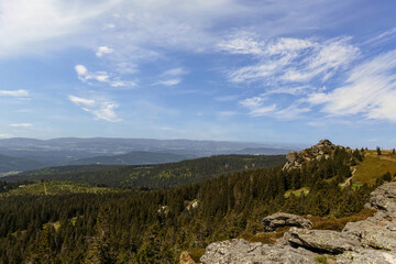 Wide view from the Arber summit in the Bavarian Forest with rocky formations, evergreen trees and a bright blue summer sky.