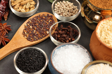 Overhead shot showcases colourful array of spices herbs on a wooden spoon pach phoron clove cardamom black seed salt pepper table spread of on dark black slate board