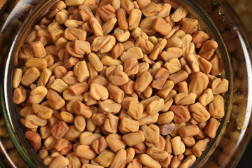 Top down flat lay view of small fenugreek seeds methi in mini glass jar on dark black slate background