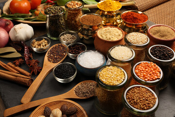 Overhead top view flat lay colourful array of spices herbs powder blue clay ceramic brass metal pot on dark black slate surface with a clean and neat appearance spice copy text space border frame