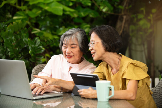 Senior women using laptop tablet outdoor garden teamwork learning technology smile coffee friendship with warm daylight create relaxed mood while sharing advice and exploring online together