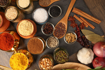 Overhead top view flat lay colourful array of spices herbs powder blue clay ceramic brass metal pot on dark black slate surface with a clean and neat appearance spice copy text space border frame