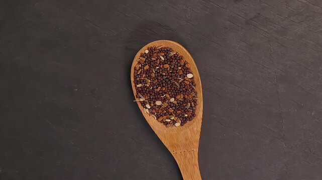 Overhead shot showcases colourful array of spices herbs on a wooden spoon pach phoron clove cardamom black seed salt pepper table spread of on dark black slate board