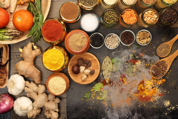 Overhead flat lay vibrant colourful spices herbs fresh produce vegetables legumes on wooden table spread splash smoking spice mix dark black slate metal clay pot palm leaf plate board copy text frame