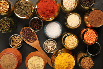 Overhead top view flat lay colourful array of spices herbs powder blue clay ceramic brass metal pot on dark black slate surface with a clean and neat appearance spice copy text space border frame