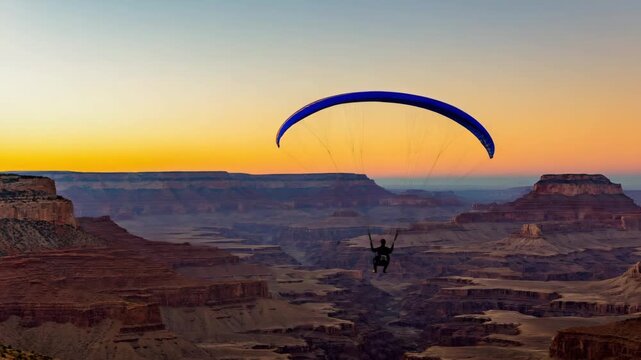 Paraglider flying over canyon at sunset
