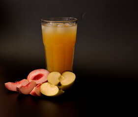 Fruit juice from peach and green apple with ice in a tall glass on a black background.